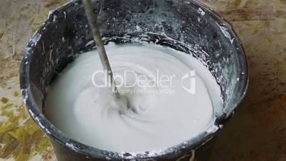 Rotating Whisk Mixer Immersed in Plaster Mix in Bucket, closeup