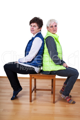 Two women sitting back to back on the chair