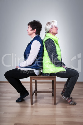 Two women sitting back to back on the chair