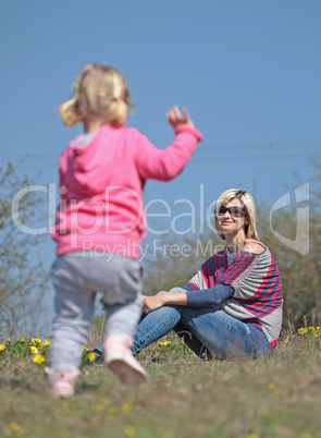 Mother and her running daughter relaxing in the nature with yellow flowers