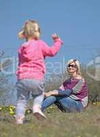 Mother and her running daughter relaxing in the nature with yellow flowers