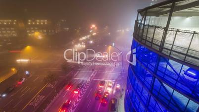 Crossroad in downtown with driving cars in the night - blue car park illuminated and foggy DSLR timelapse