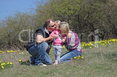 Happy mother, father kissing theirs daughter in the nature