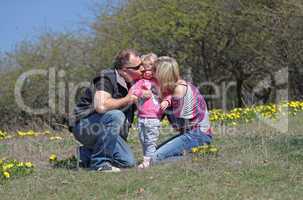 Happy mother, father kissing theirs daughter in the nature