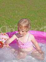 Little blonde girl playing in a water-filled kiddie pool