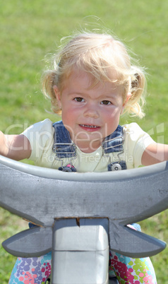 Little blonde girl riding on a grey wooden bull outdoors