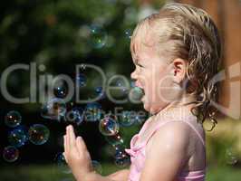 Happy little girl playing with soap bubbles int he garden