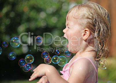 Happy little girl playing with soap bubbles int he garden