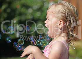 Happy little girl playing with soap bubbles int he garden