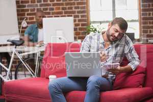 Man using laptop and mobile phone on couch in office