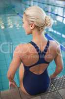 Rear view of a fit female swimmer sitting by pool