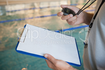 Swimming coach looking at his stopwatch by pool