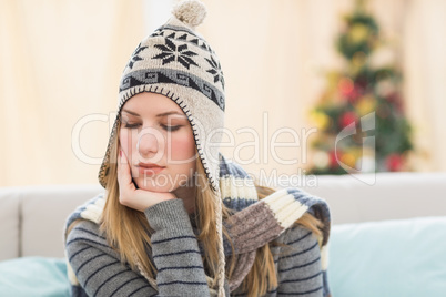 Thoughtful pretty brunette with winter hat sitting on couch