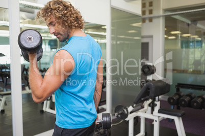 Handsome young man exercising with dumbbell in gym