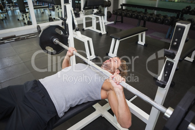 Young muscular man lifting barbell in gym