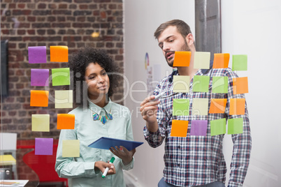 Team using digital tablet by sticky notes on window