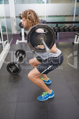 Side view of muscular man lifting barbell in gym