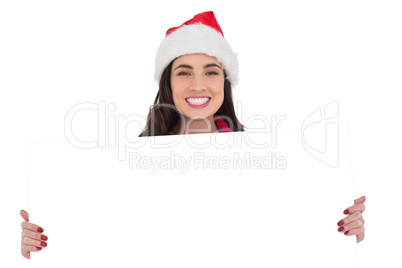 Smiling brunette in santa hat showing white poster