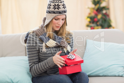 Blond woman opening a gift sitting on a sofa