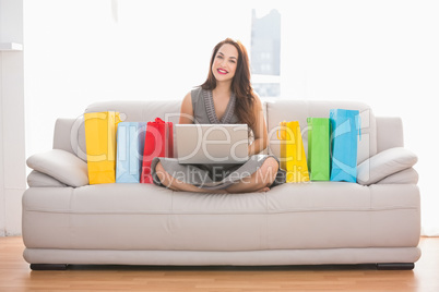 Smiling brunette shopping online with laptop on the couch