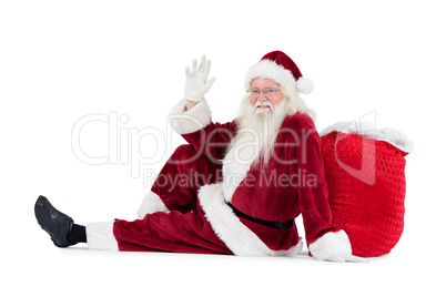 Santa sits leaned on his bag and waves
