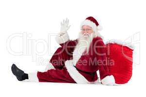 Santa sits leaned on his bag and waves