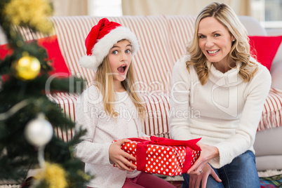 Festive mother and daughter on the couch with gift
