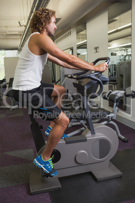 Side view of man working out on exercise bike at gym
