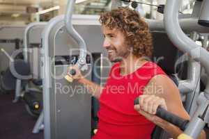 Handsome smiling man working on fitness machine at gym