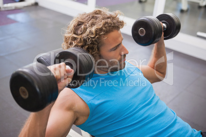 Side view of man exercising with dumbbells in gym