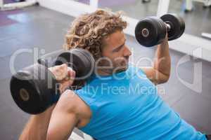 Side view of man exercising with dumbbells in gym