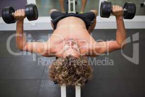 Shirtless man exercising with dumbbells in gym