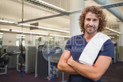 Smiling handsome trainer with arms crossed in gym