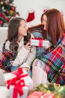 Festive mother and daughter wrapped in blanket with gifts