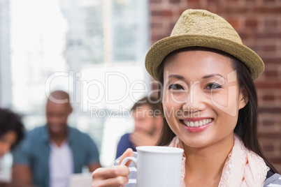Woman holding coffee cup with colleagues behind in office