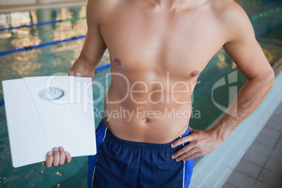 Mid section of a shirtless fit swimmer with weighing scales by p