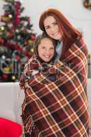 Festive mother and daughter wrapped in blanket