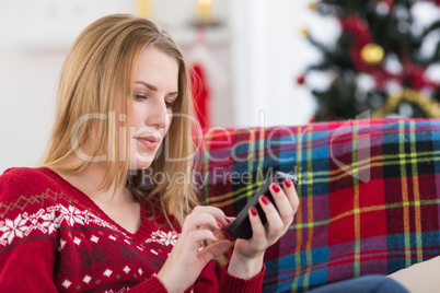 Pretty blonde sitting on the couch texting on the phone