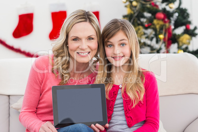 Festive mother and daughter showing tablet screen