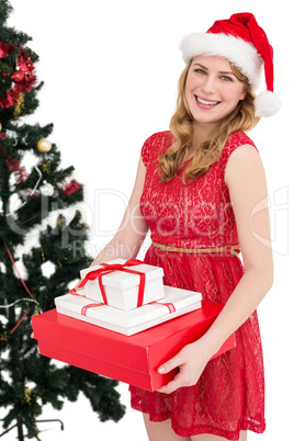 Blonde holding pile of gifts with christmas tree behind her