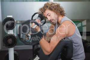 Side view of muscular man lifting barbell in gym