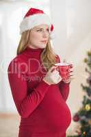 Festive pregnant woman holding mug while standing
