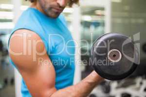 Mid section of man exercising with dumbbell in gym