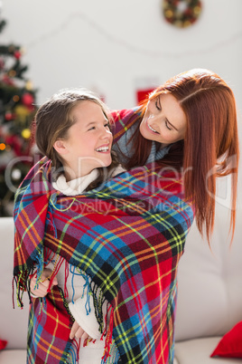 Festive mother and daughter wrapped in blanket