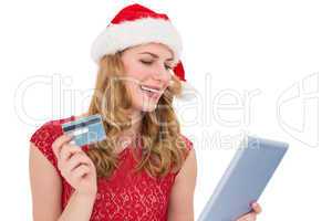 Festive blonde woman using her credit card and tablet pc