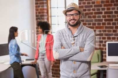 Man with arms crossed and colleagues behind in office