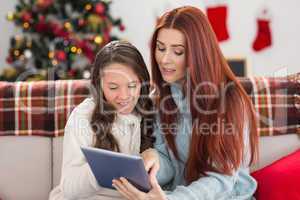 Festive mother and daughter using tablet on the couch