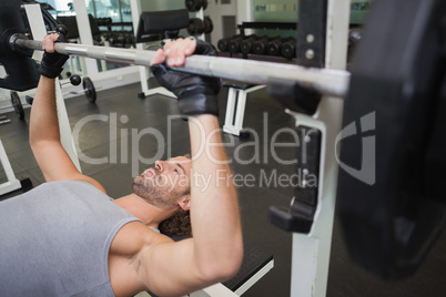 Young muscular man lifting barbell in gym