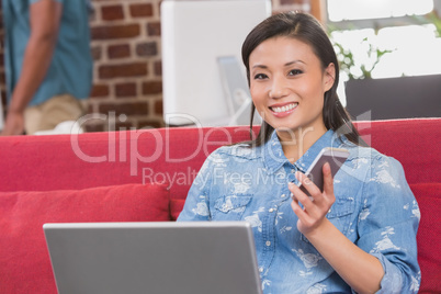 Casual woman using laptop and mobile phone on couch