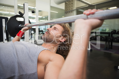 Young muscular man lifting barbell in gym